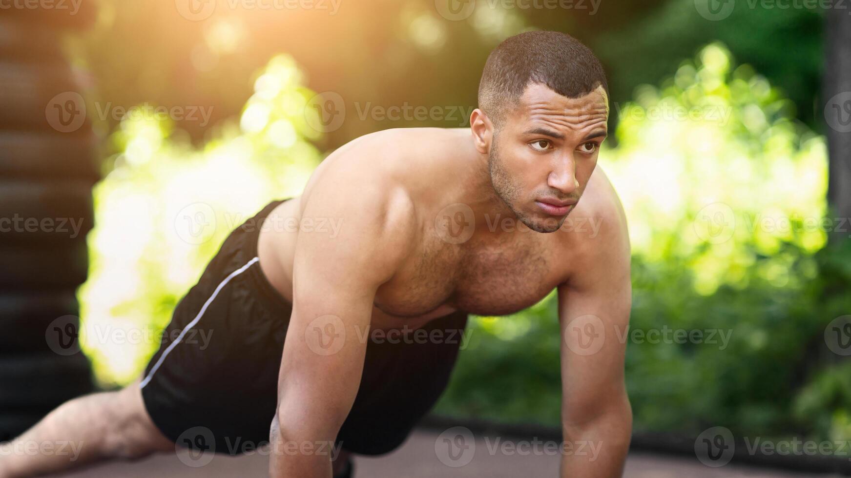 Millennial black guy doing push ups on asphalt road at urban park in morning photo
