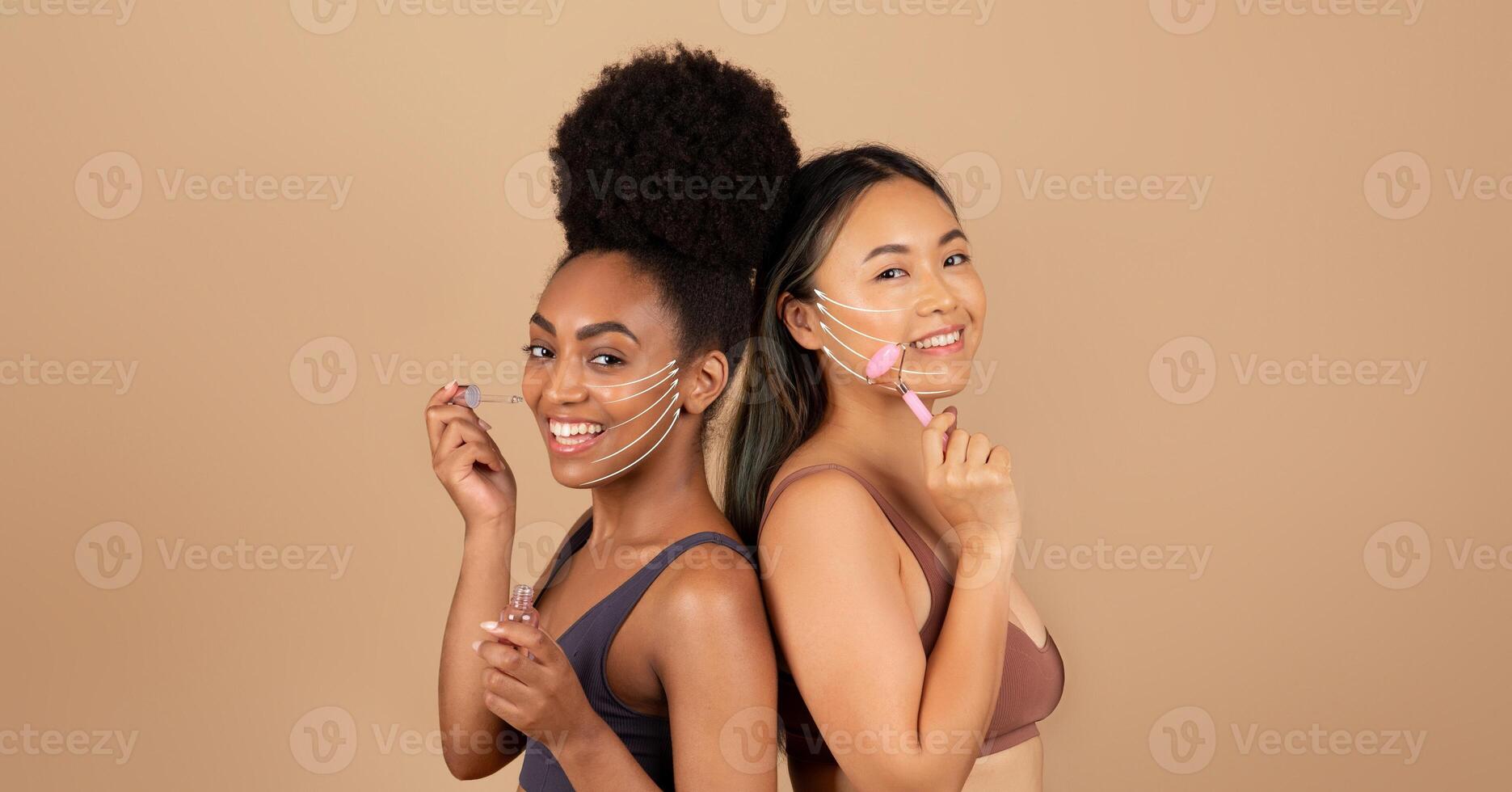 Two multiethnic women stand back to back, smiling as they enjoy a rejuvenating skin care session. They use facial massage tools to enhance their anti-aging routine in a serene environment. photo