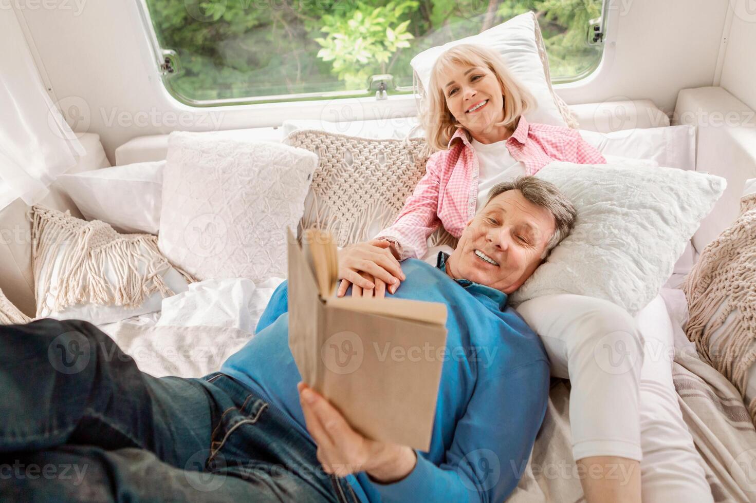 Happy married couple relaxing on bed and reading interesting book inside of camper van photo