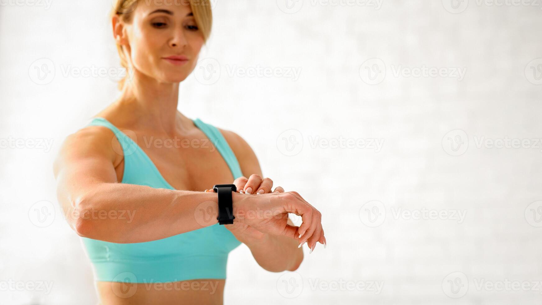 Exercises and biological rhythms. Attractive fitness adult woman in sportswear checks fitness tracker in bright living room interior, panorama, free space photo