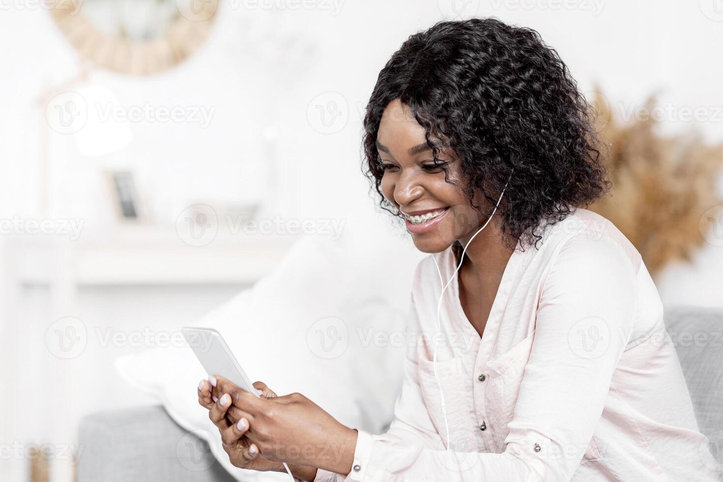 Free Time At Home. Happy Black Woman Listening Music On Smartphone, Using Earphones, Watching Videos, Browsing Internet While Resting On Couch In Living Room, Enjoying Weekend Relax, Free Space photo