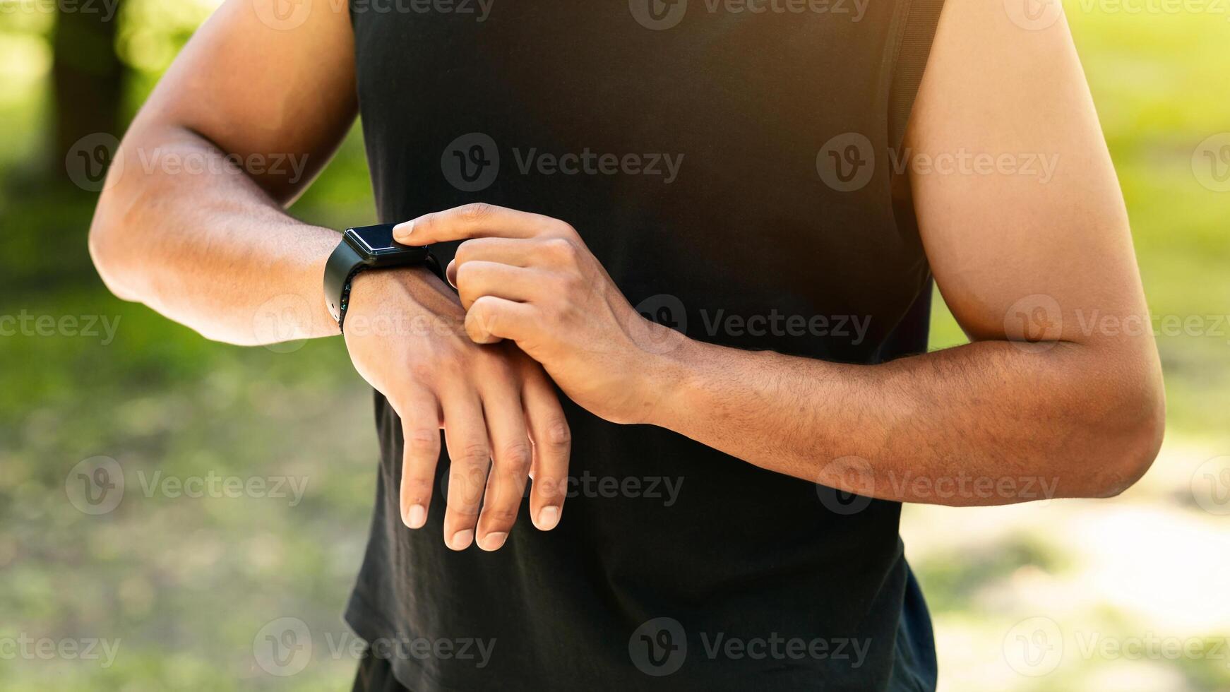 Closeup view of young guy checking his smartwatch or fitness tracker during training outdoors, panorama photo