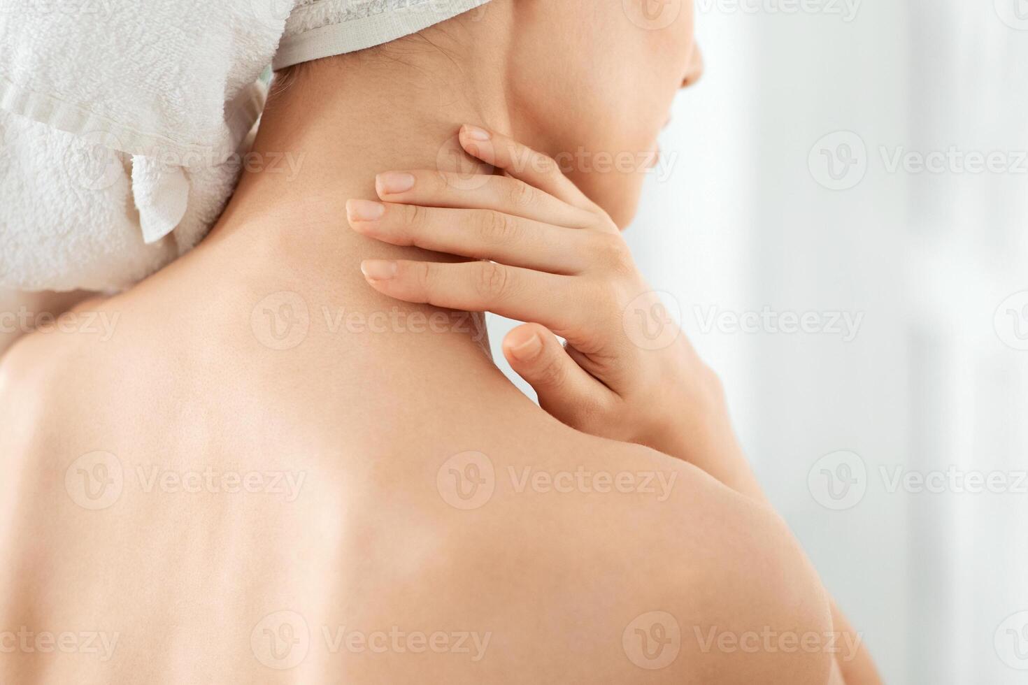 Body care concept. Cropped of unrecognizable woman wrapped in towel using body nourishing cream or lotion. Back view of young lady using moisturizer for her skin after shower, copy space, closeup photo