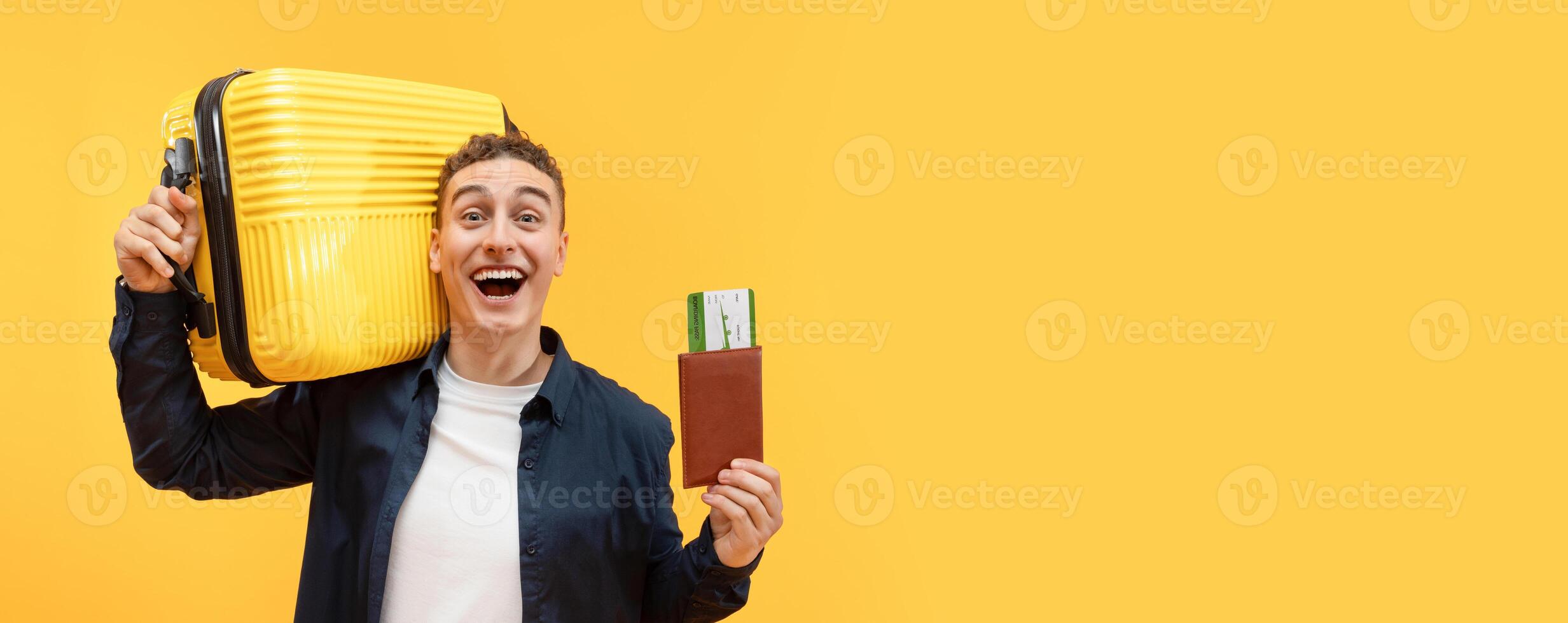 Excited young guy tourist with suitcase and passport, flight tickets cheerfully smiling isolated over yellow studio background, enjoying hot traveling offer, going vacation photo