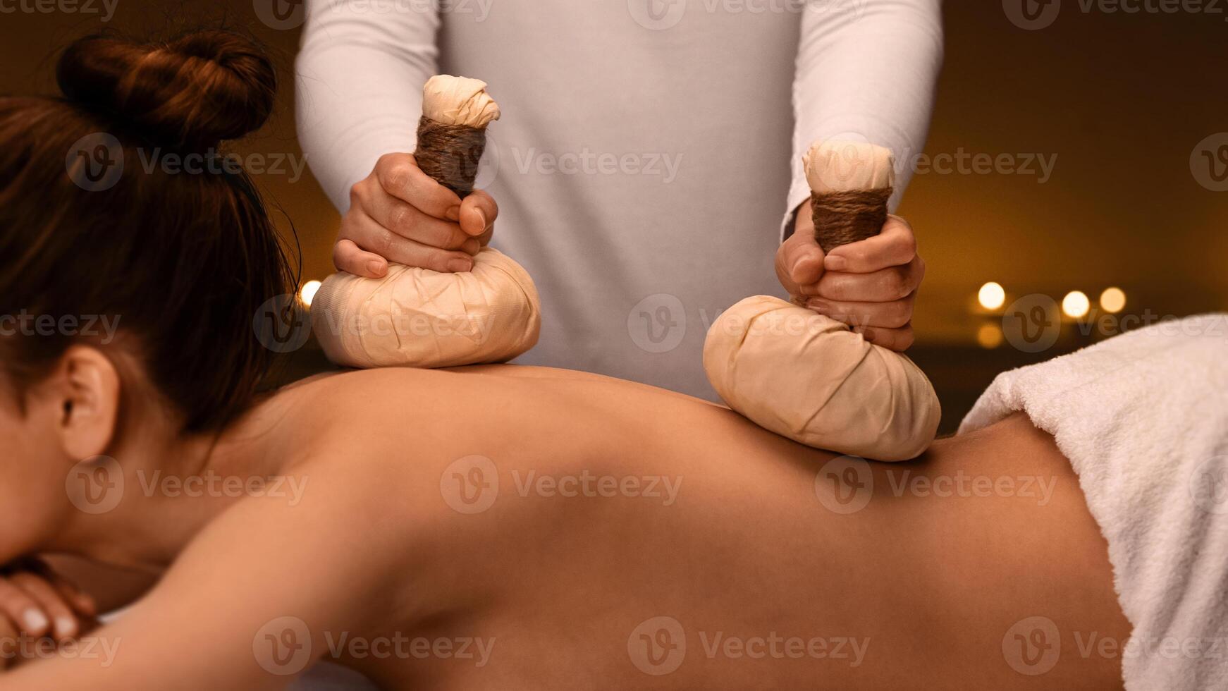 Herbal massage. Therapist making body massage to young woman with herbal compress balls, spa interior photo