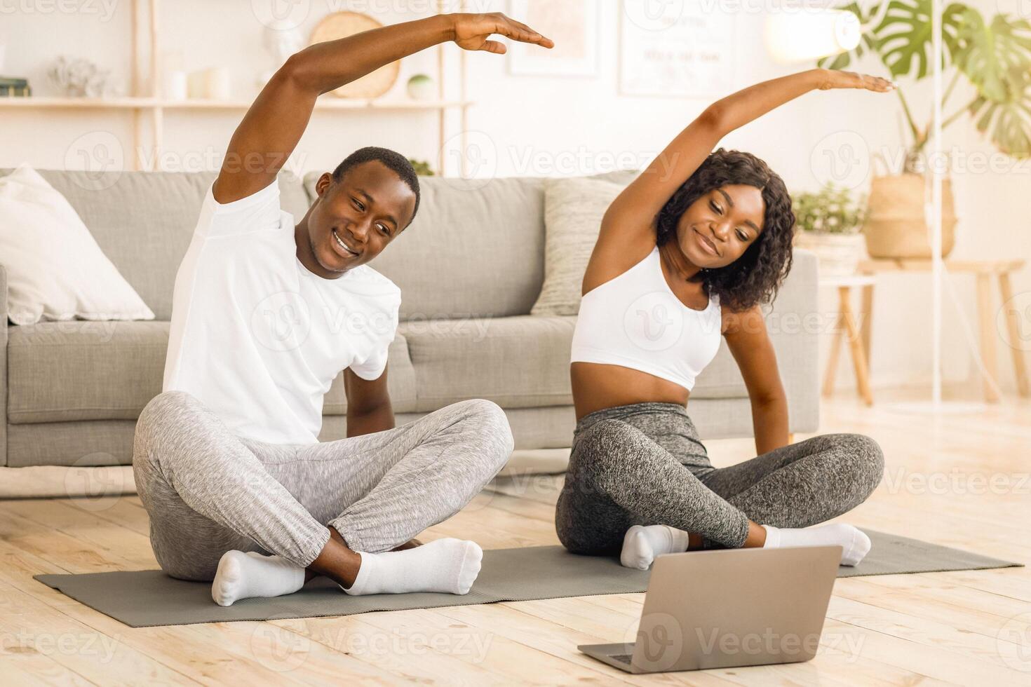 Sporty african couple stretching at home together, watching online lesson on laptop photo