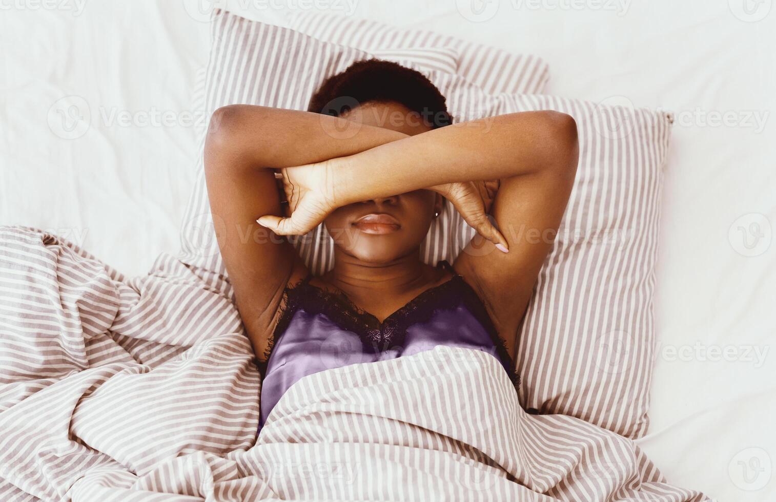 Nightmares or depression. Sleepless young woman suffering from insomnia, lying on bed, covering eyes with hands, trying to sleep, feeling headache or migraine on bed in bedroom, top view, empty space photo