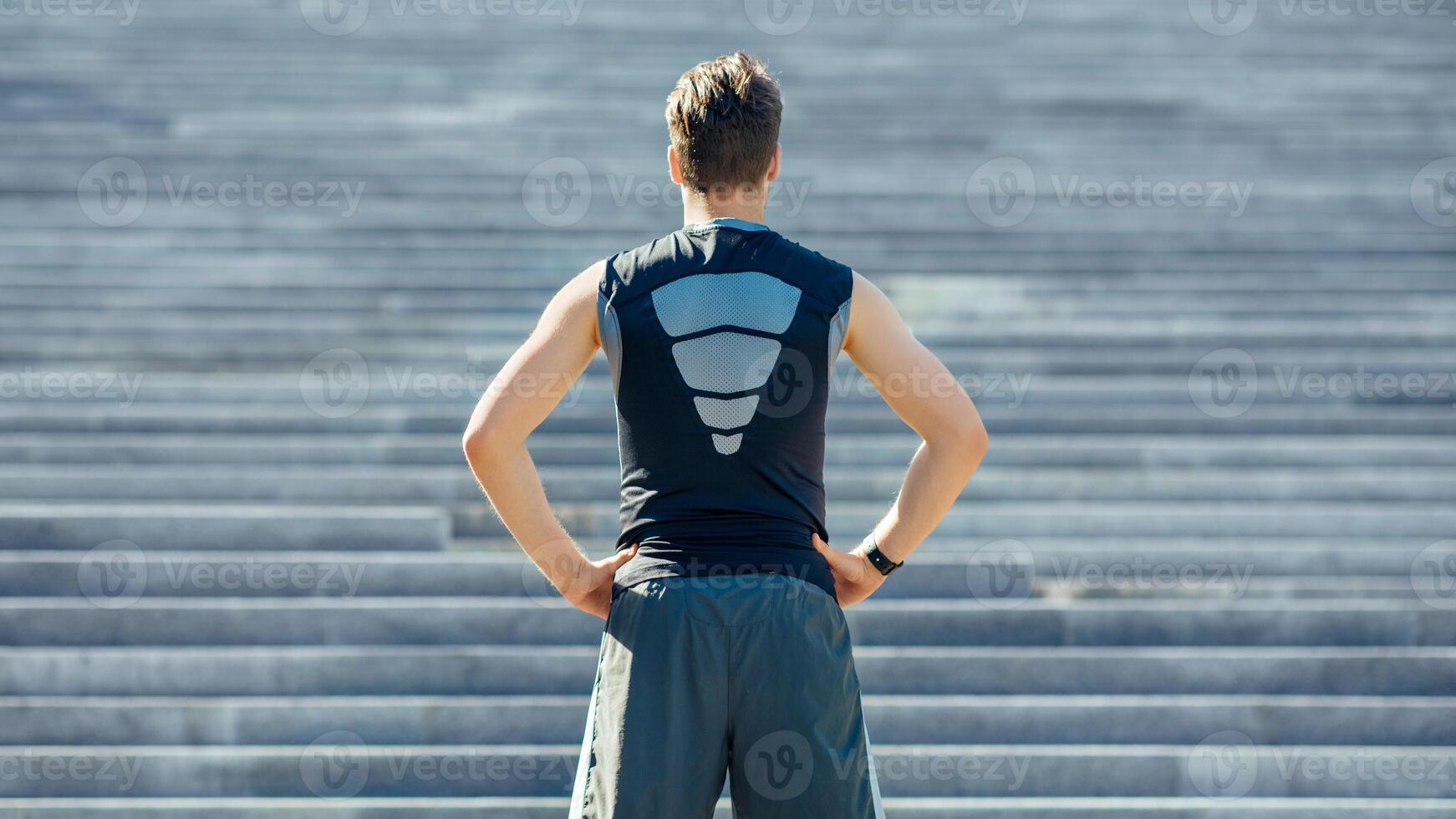 Training on stairs. Guy in sportswear, with fitness tracker at the beginning of the path and looking at steps, back, free space photo