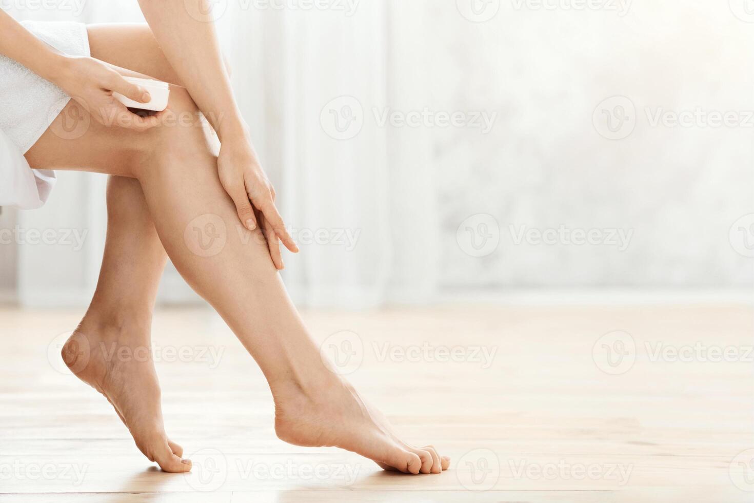 Closeup of woman applying cream on her legs after shower at home, empty space photo