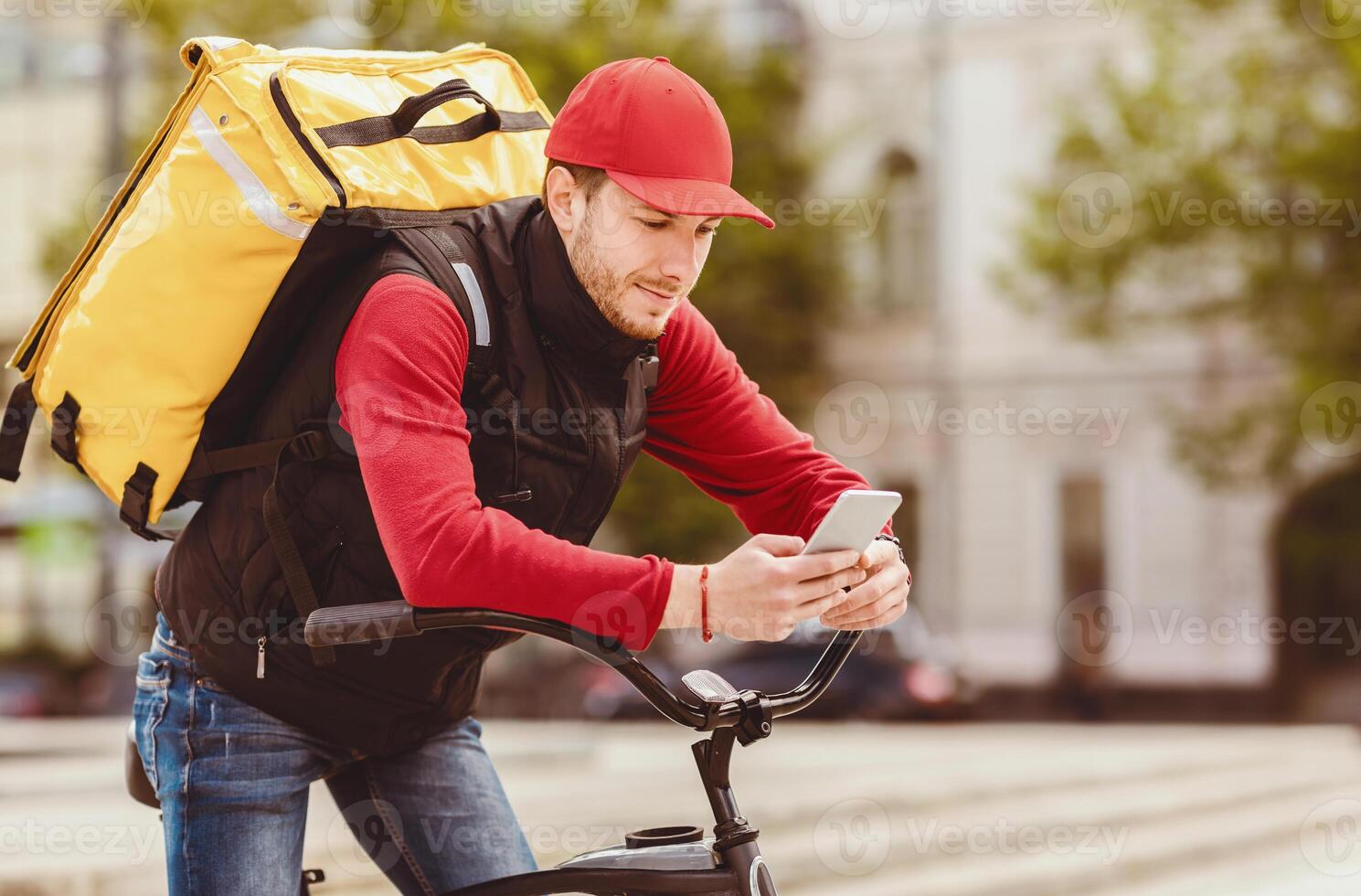 Delivery App. Courier Using Mobile Phone Delivering Food Order On Bike In City Outdoors. Copy Space photo