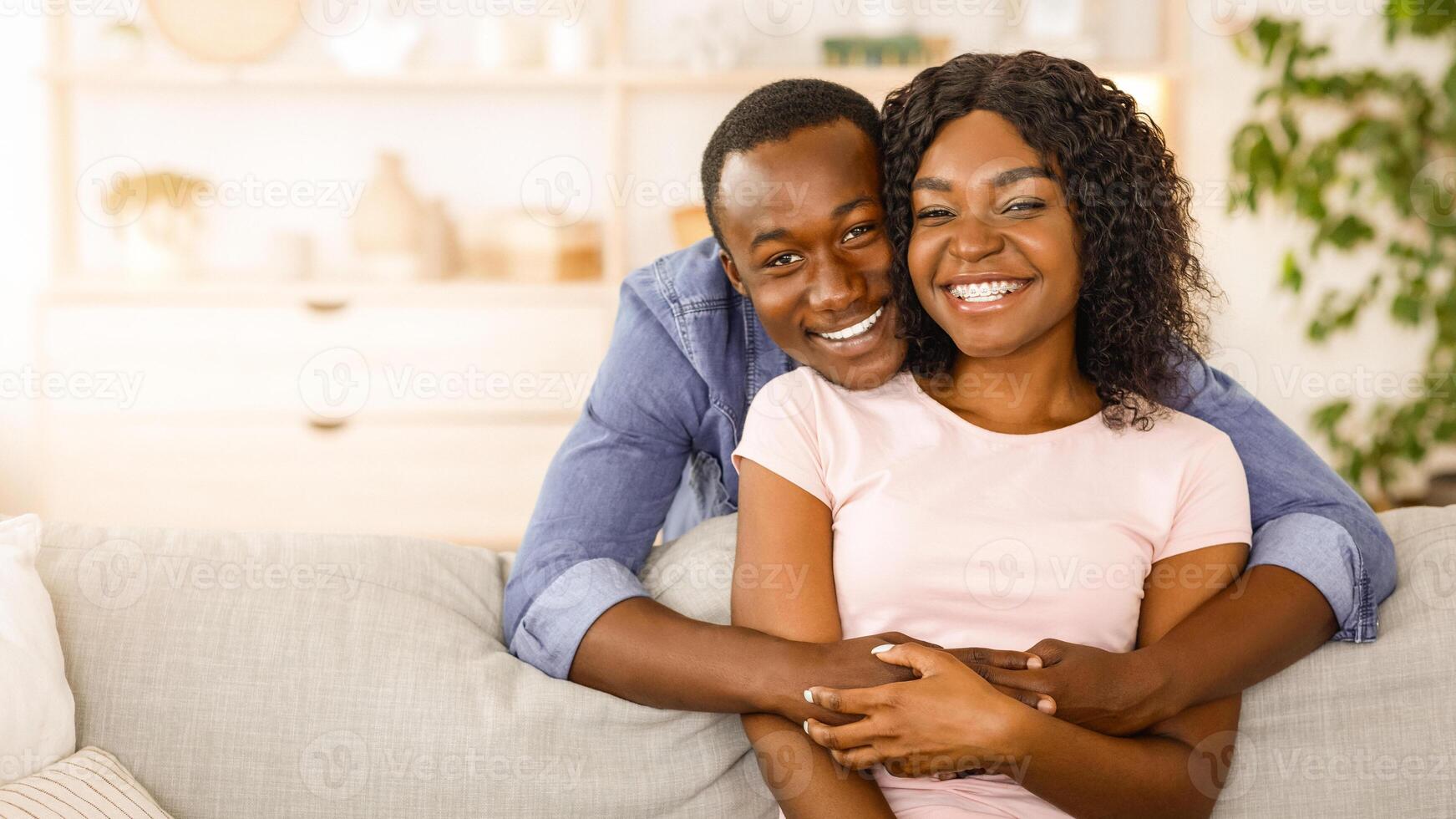 Cheerful african man hugging his smiling wife from behind, spending time together at home, empty space photo