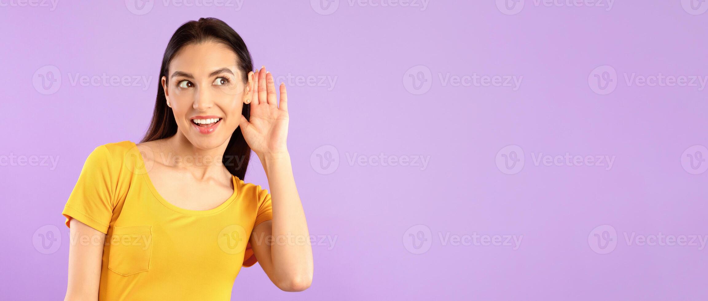 Eavesdropping Concept. Curious girl holding her hand near ear and listening carefully isolated over purple wall, copyspace photo