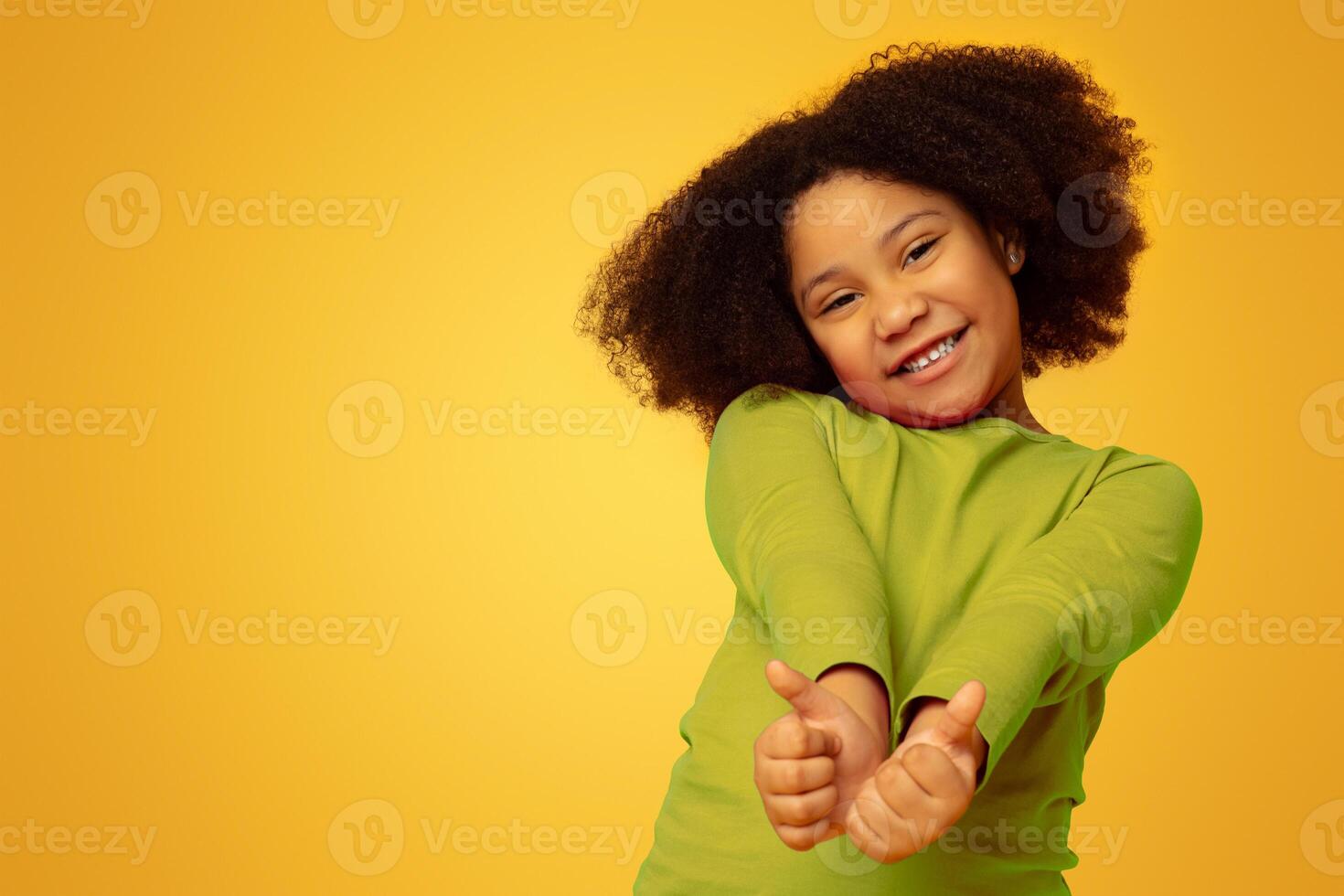 Everything is great. Positive cute little girl gesturing thumbs up and smiling at camera, yellow studio background with empty space photo