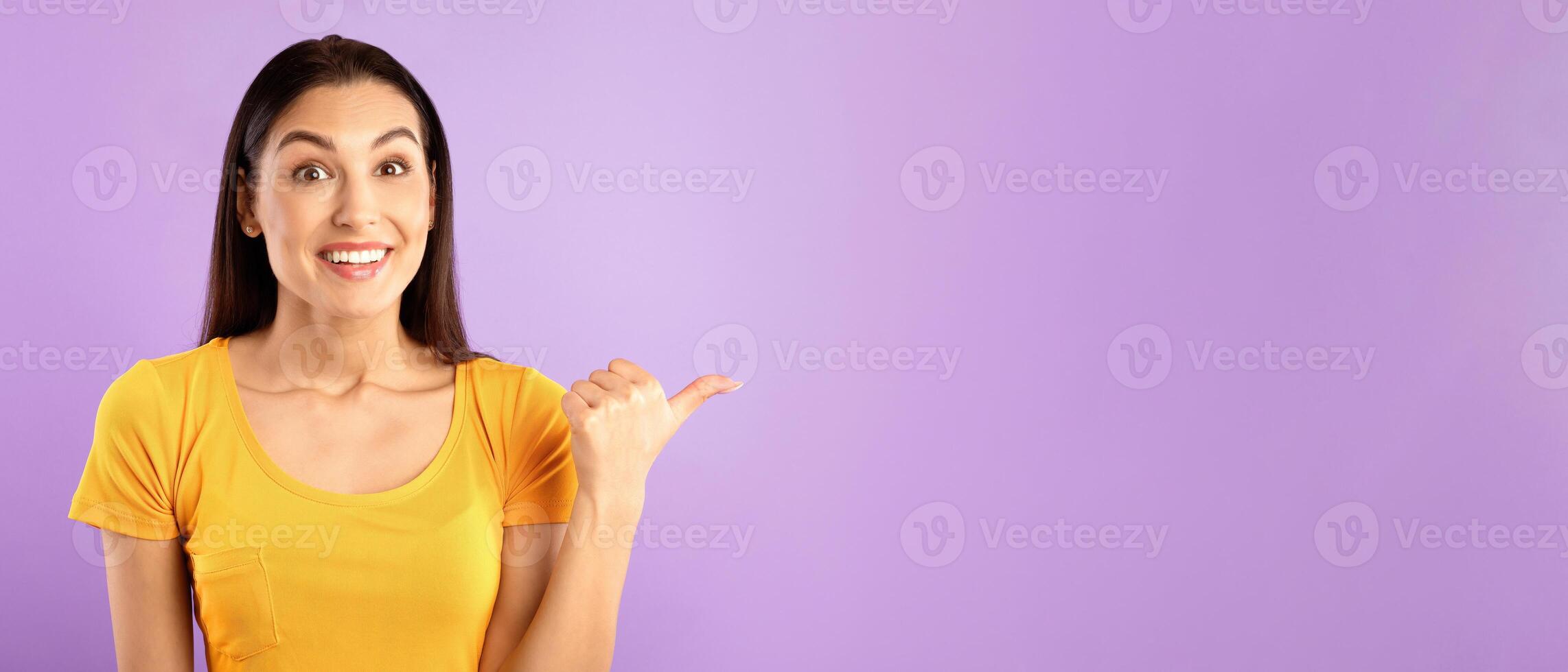 Check This. Smiling girl pointing aside at copyspace with thumb up isolated over pastel purple studio wall photo