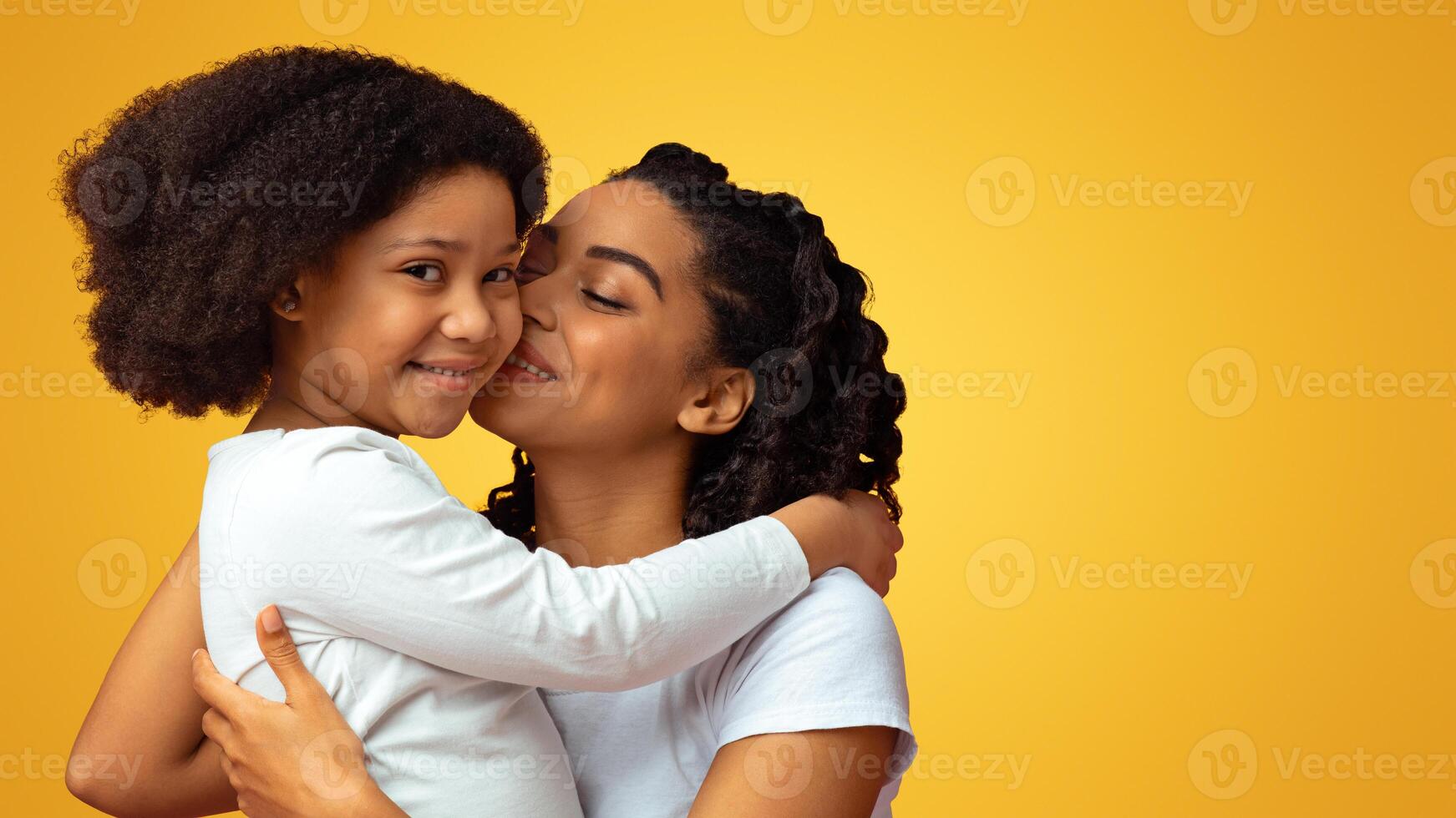 Mother's Warmth. Loving African Woman Tenderly Kissing Her Cute Little Daughter Isolated On Pink Background With Free Space photo