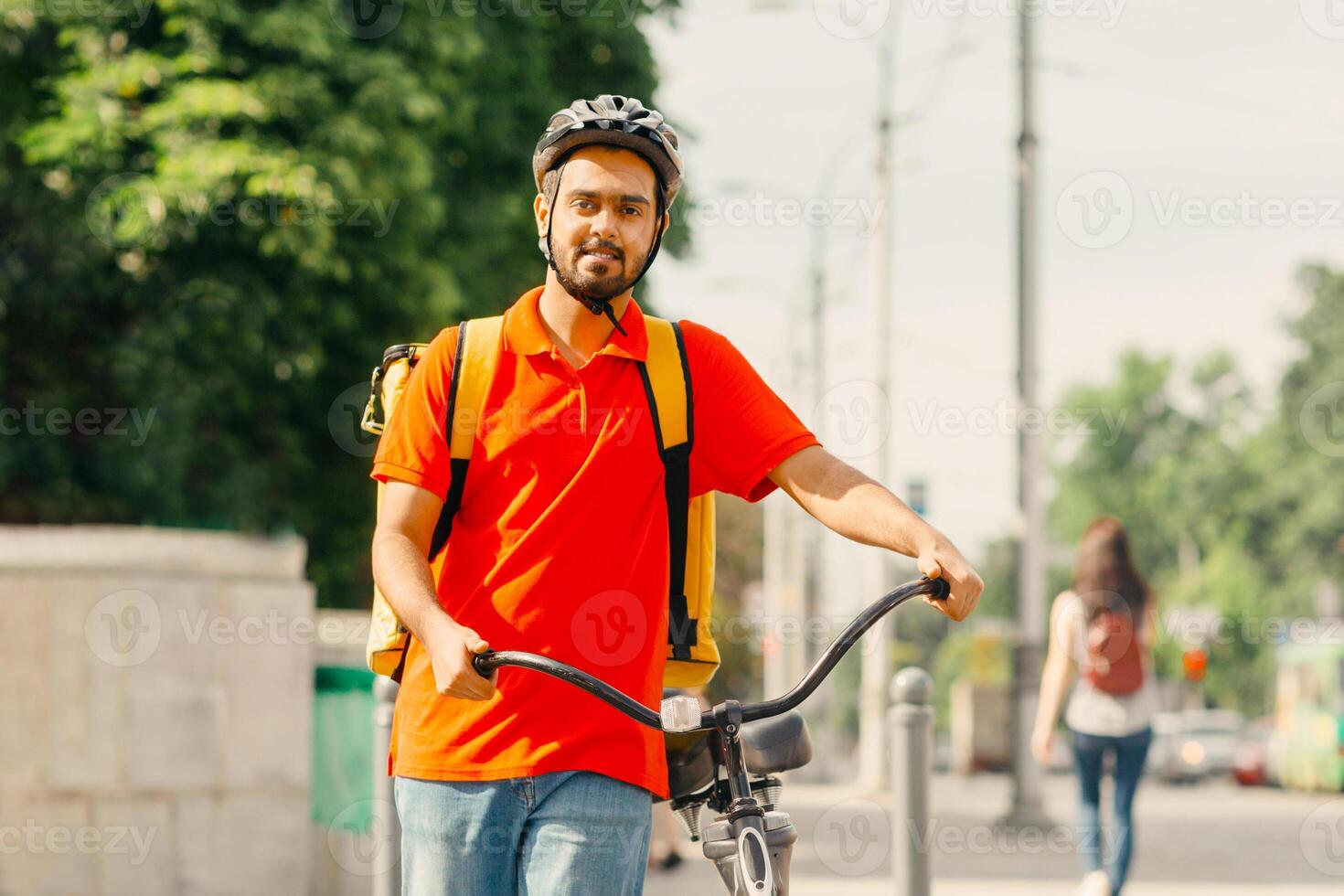 Traffic light and pedestrian crossing in city. Friendly young man courier in helmet with big yellow bag and bicycle, walks along the road in city, copy space photo