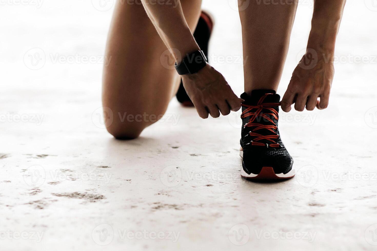 Health care and exercise in middle age. Muscular lady in sports uniform and fitness tracker ties shoelaces on sneakers on floor with water bottle for morning workout, indoor, free space, cropped photo