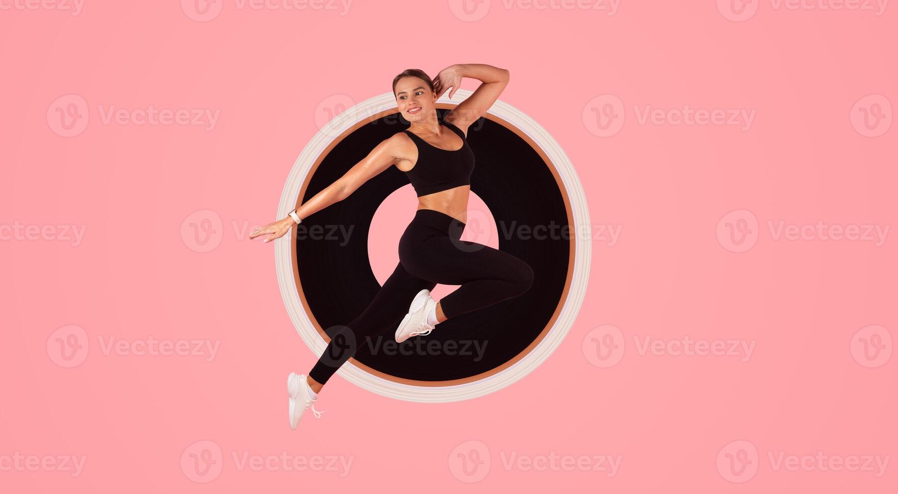 Fitness Lifestyle. Motivated Sporty Lady In Fitwear Jumping In Air Over Pink Background In Studio, Athletic Young Woman Making Jump Exercises And Looking Aside, Enjoying Cardio Workout, Full Length photo