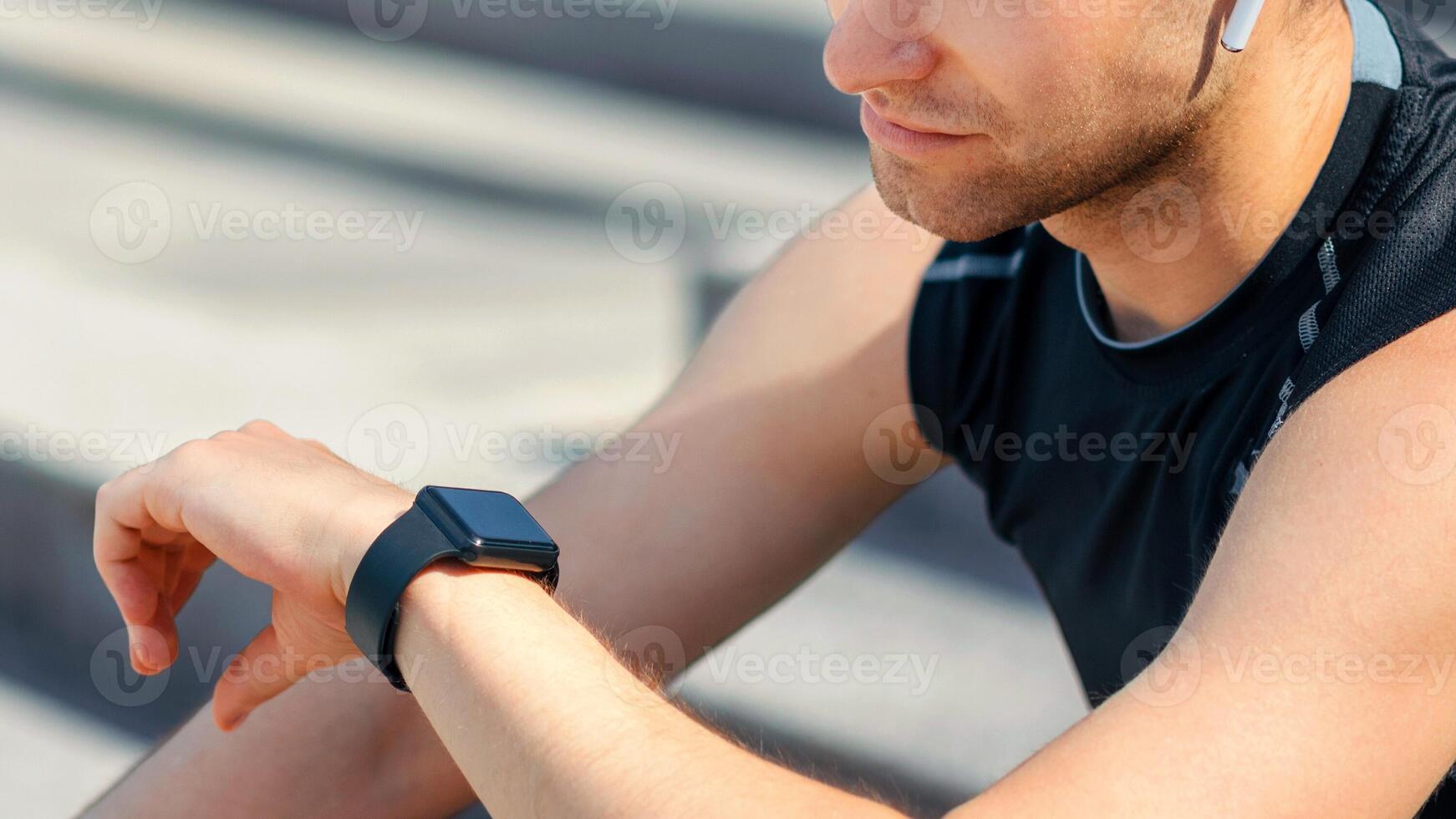 Checking biological rhythms of body. Guy in sportswear looking at fitness tracker on arm, sitting on steps, panorama, cropped, free space photo