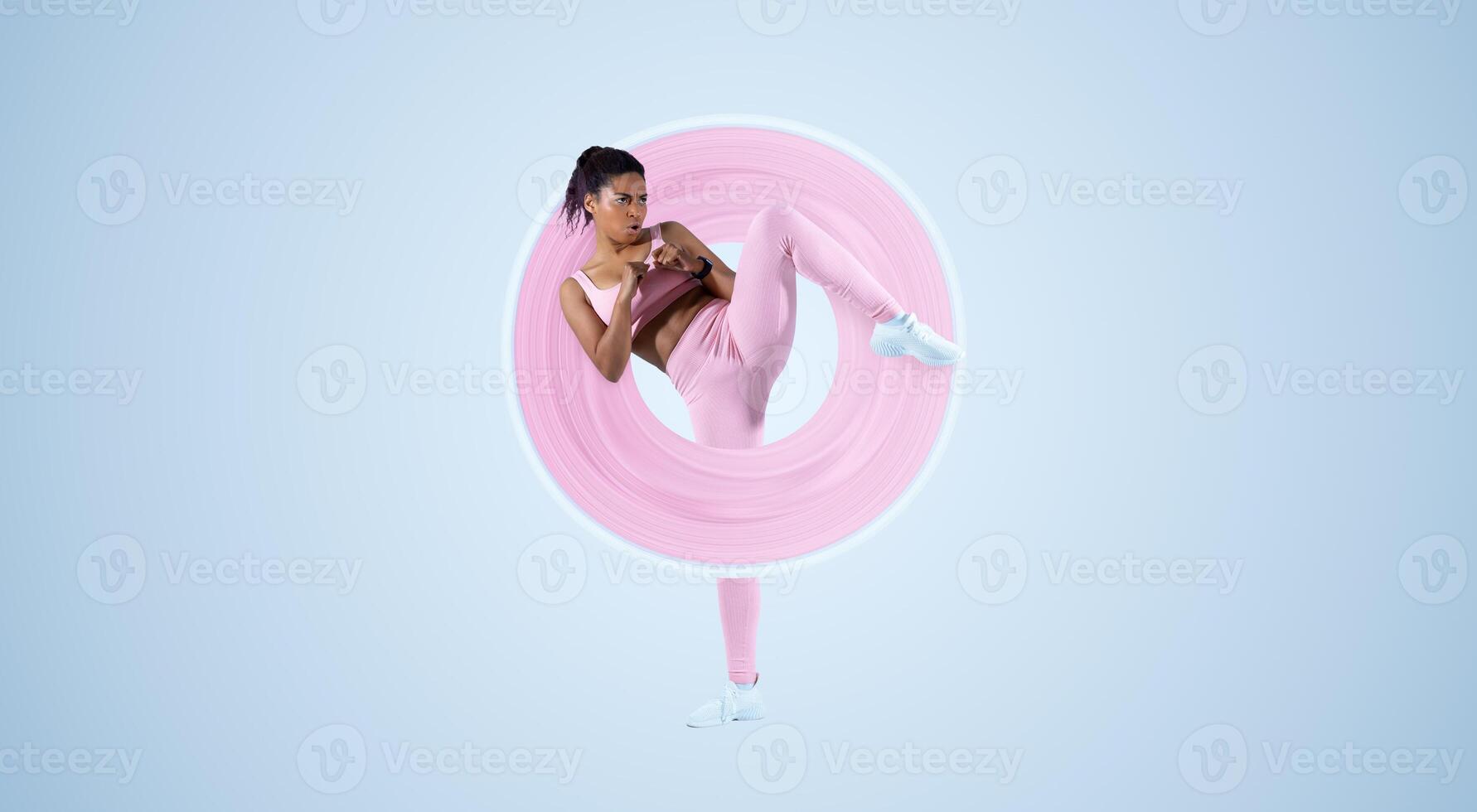 Lady trainer showing kick exercise for self defense by legs on blue studio background, copy space. African American woman training in sportswear in studio photo