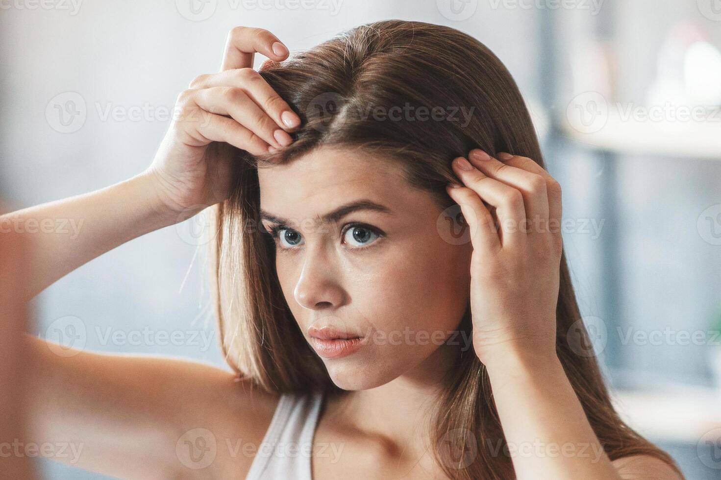 Millennial girl with hair loss problem looking in mirror at home photo