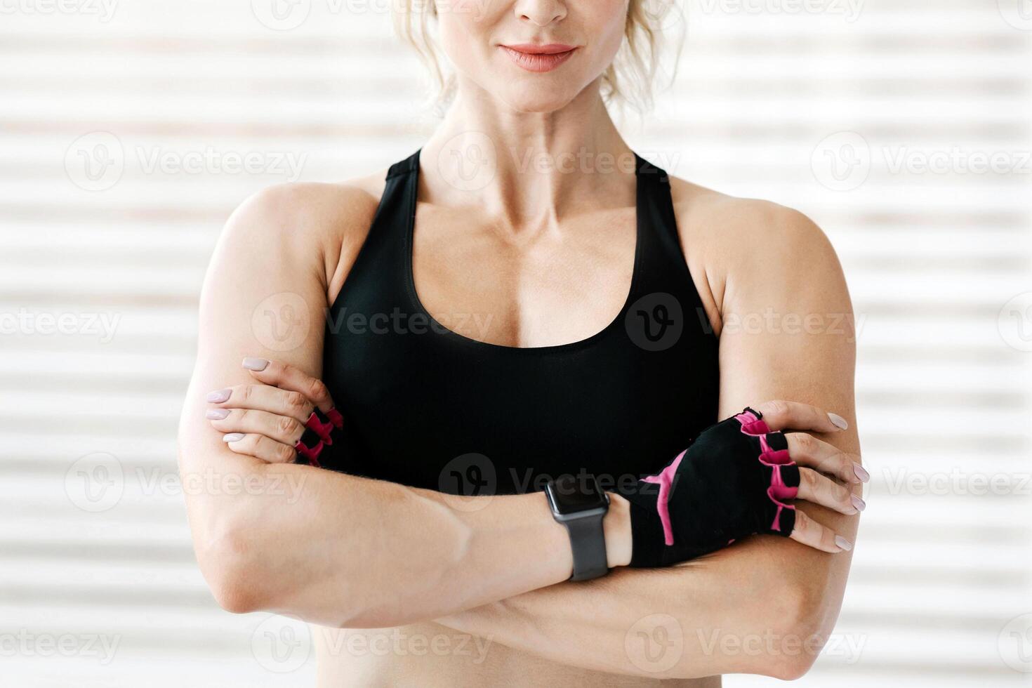 Fitness model and motivation. Friendly adult woman in sportswear with smart watch with arms crossed, demonstrates muscles at home or gym, copy space photo