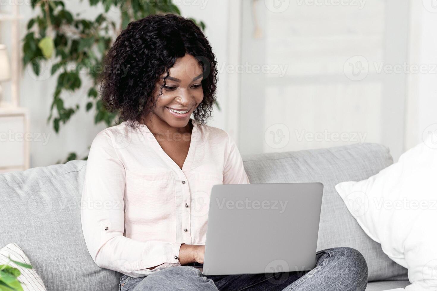Remote Work. Joyful Black Woman Working On Laptop On Couch At Home, Using Computer For Freelancing, Free Space photo