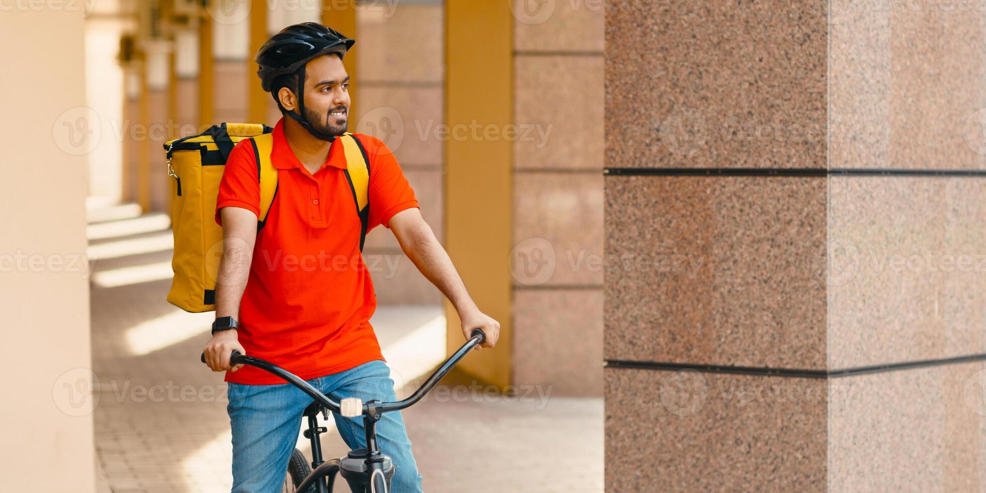Environmentally friendly urban transport for delivery. Bearded courier in helmet, in uniform and yellow backpack rides bicycle in city, panorama, free space photo