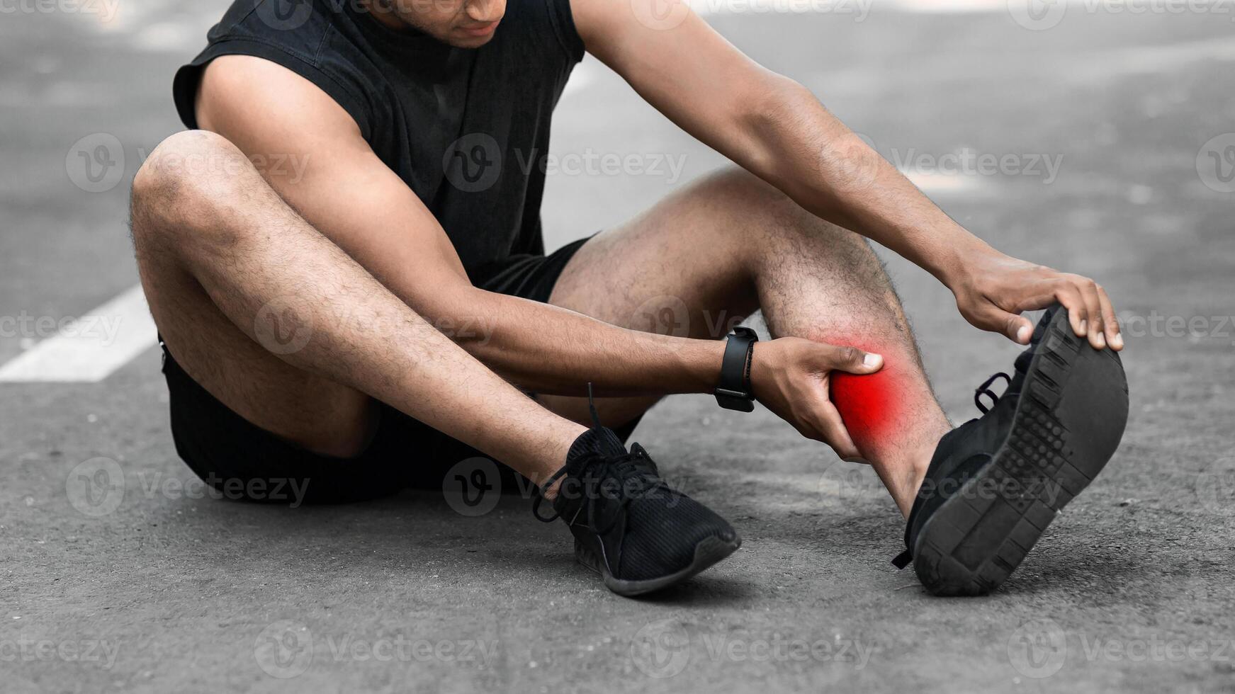 Sports injury. African American runner sitting on jogging track and feeling pain in his ankle, panorama photo