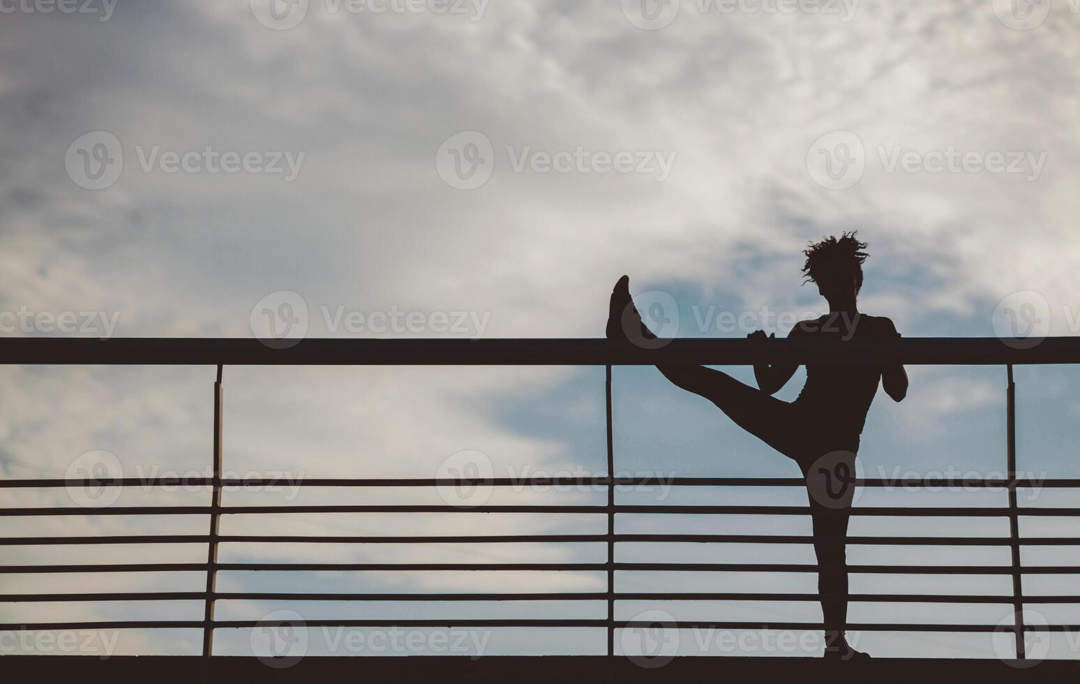 Training in city. Silhouette of african american girl doing stretching legs on sky background, free space photo