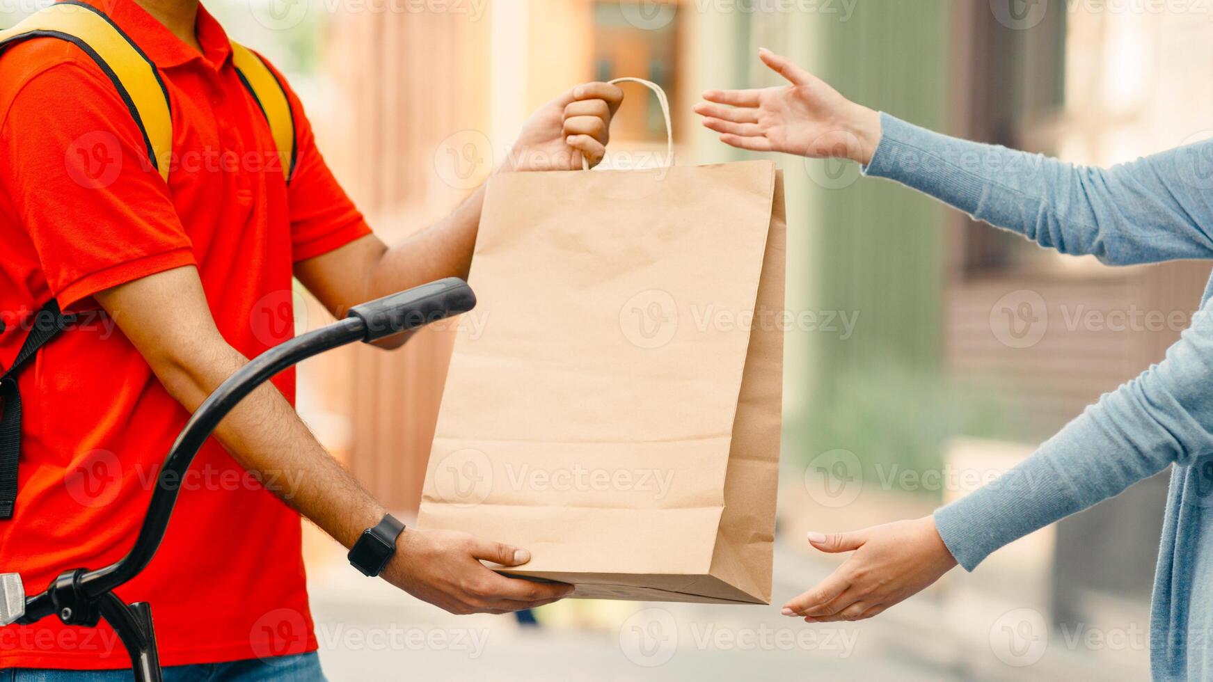 Online shopping and delivery by courier on bike. Man with backpack and smart watch gives paper bag to client, outside, side view, free space photo