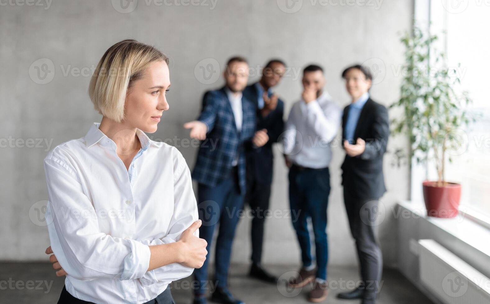 Sexism And Bullying At Work. Unhappy Victimized Business Lady Standing While Her Male Coworkers Whispering Behind Her Back In Modern Office. Workplace Discrimination Problem, Female Rights. Free Space photo