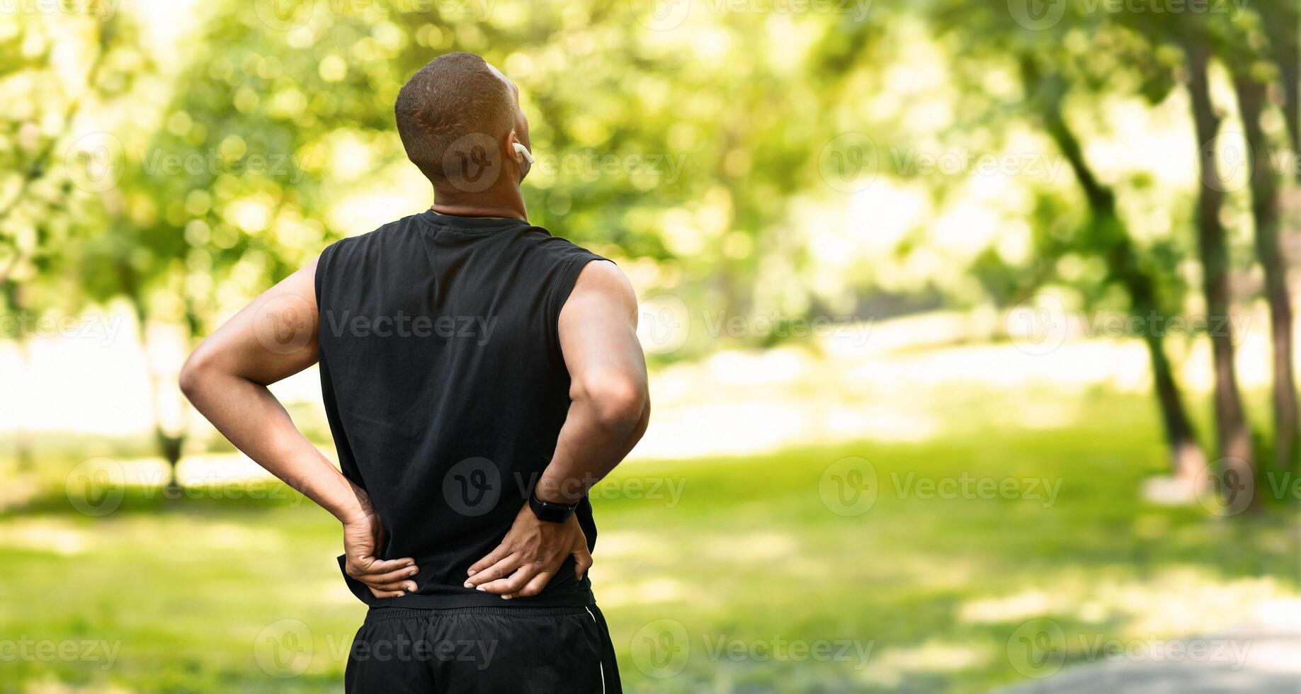 Millennial guy in sportswear suffering from back pain wgilejogging at park, copy space photo