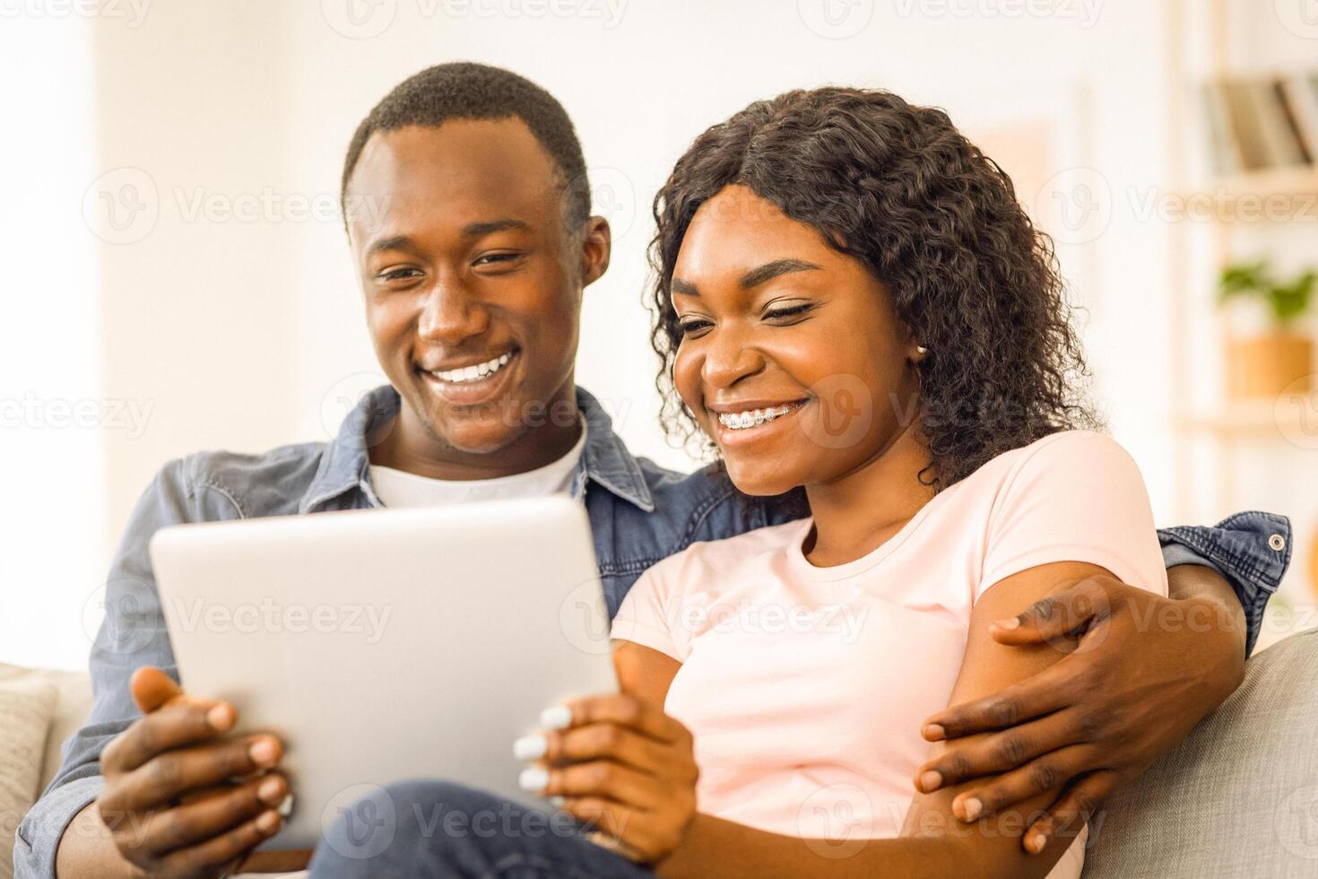 Closeup of smiling young african man and woman using digital tablet while resting at home photo
