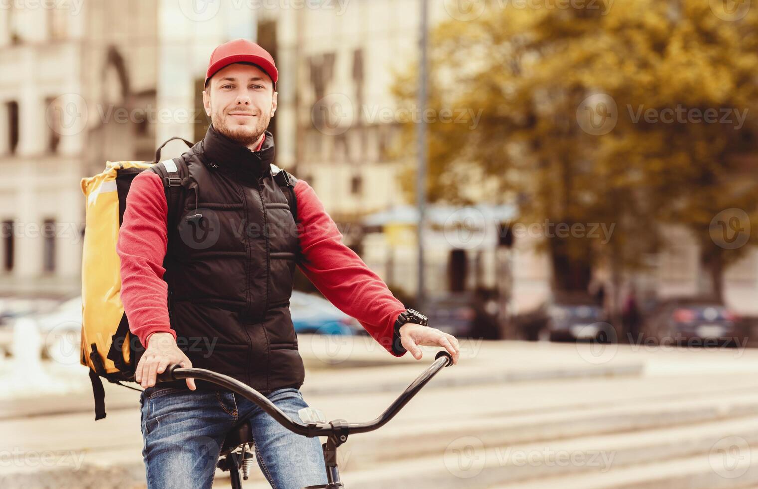Courier Man On Bike Standing With Bag Delivering Food In City, Smiling To Camera. Free Space For Text photo