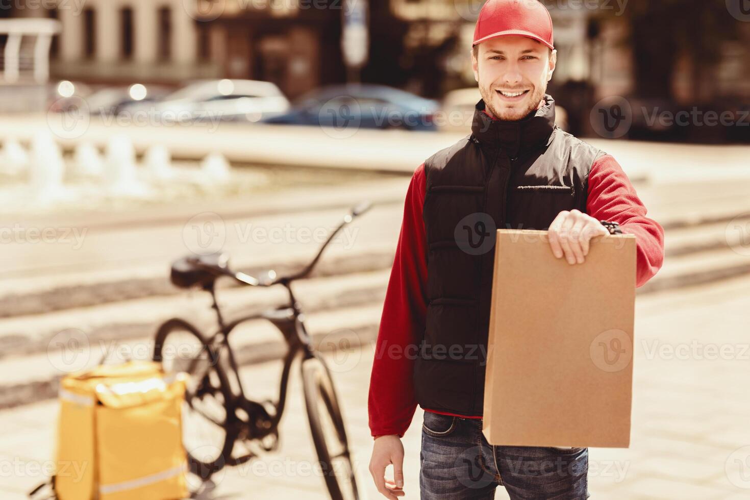 Your Offer. Courier Guy Holding Package Smiling To Camera Delivering Food Standing In Urban Area Outside. Free Space For Text photo