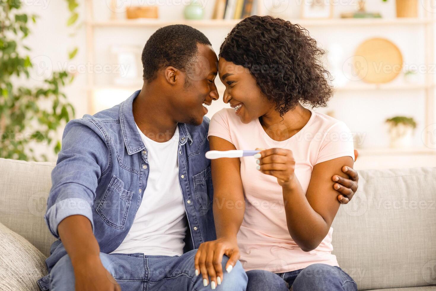 Happy pregnant african couple with pregnancy test at home, hugging and looking at each other, free space photo