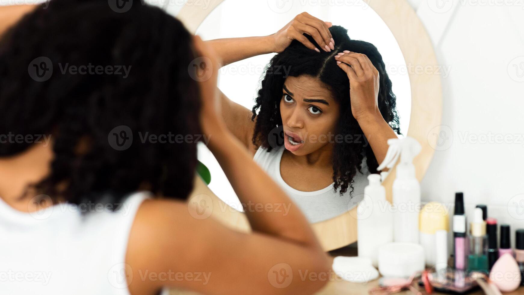 Dandruff Problem. Sad Black Woman Looking At Her Hair Roots With Flaky Scalp In Mirror, Sitting At Dressing Table, Over Shoulder View photo