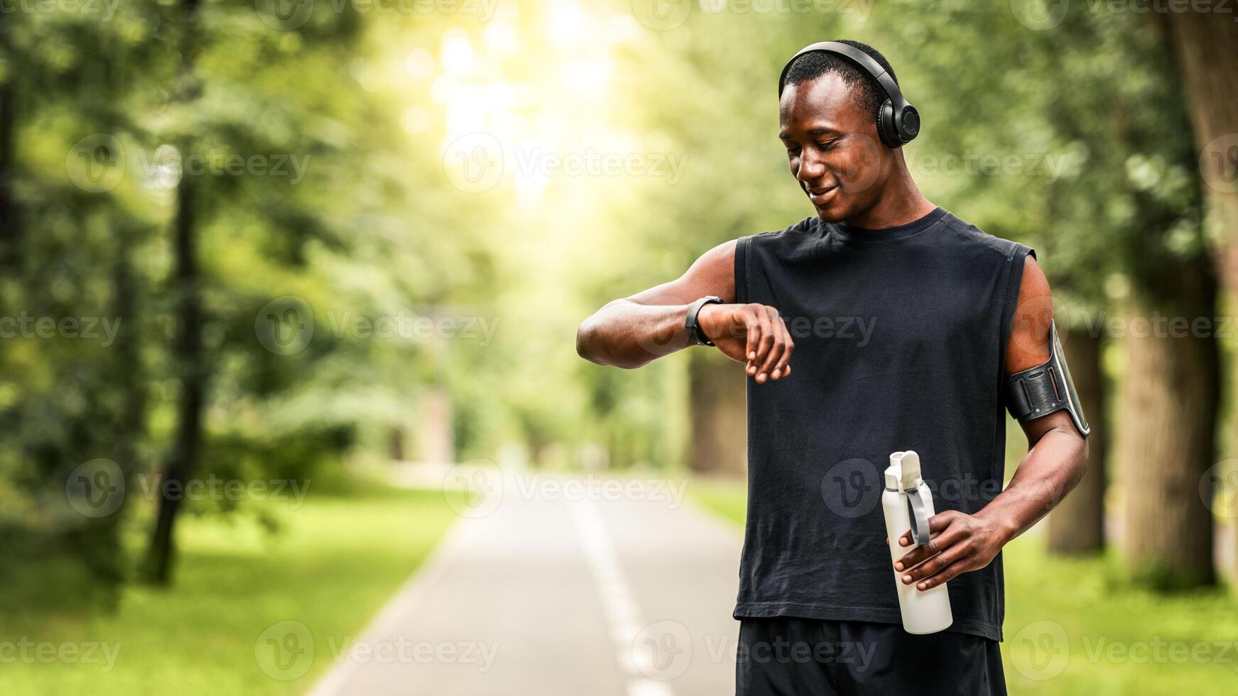 Modern technologies and active lifestyle. African sportsman working out with fitness bracelet, drinking water, blurred park background, copy space photo