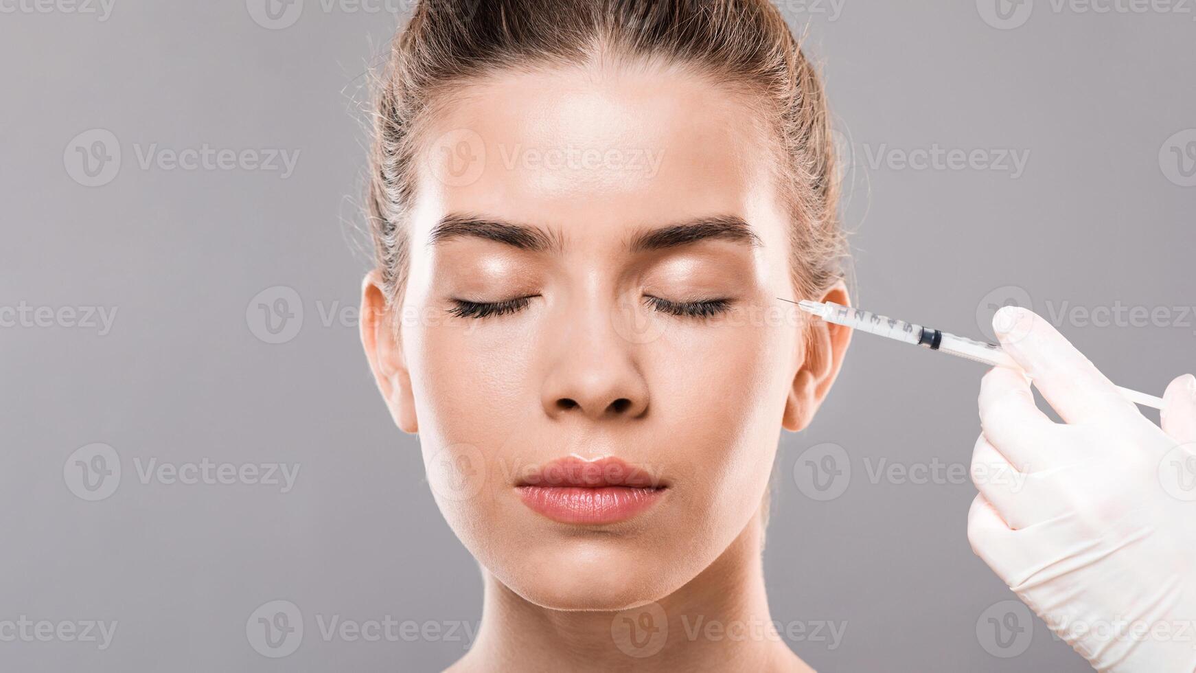 Closeup of young lady having injections for eye wrinkles, grey background, free space photo