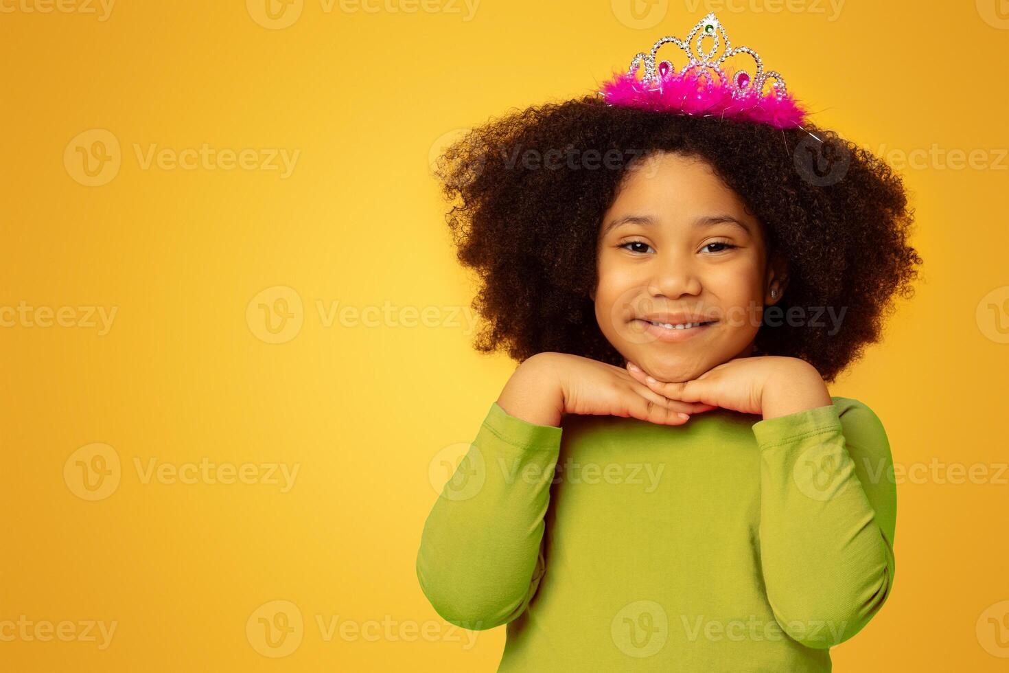 Adorable Little Afro Girl Wearing Princess Crown And Smiling At Camera, Posing On Yellow Background In Studio, Empty Space photo