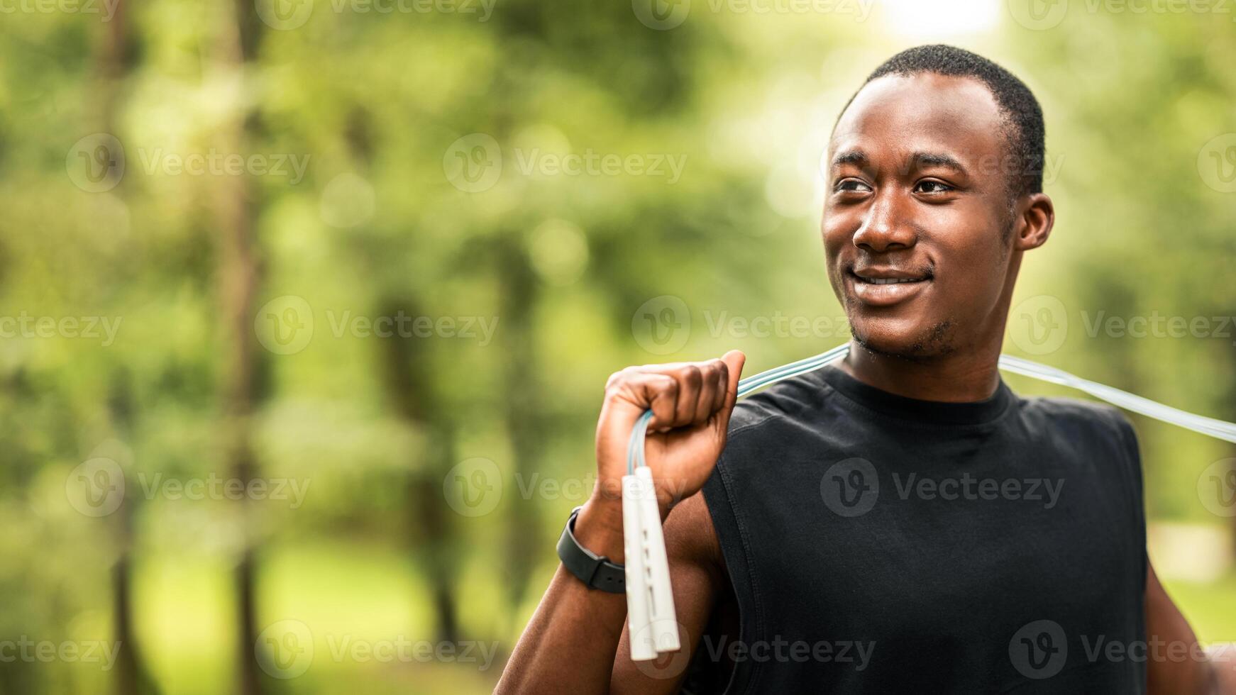 Sport tools and equipment concept. Smiling sporty african guy with jumping rope training at park, looking at free space photo