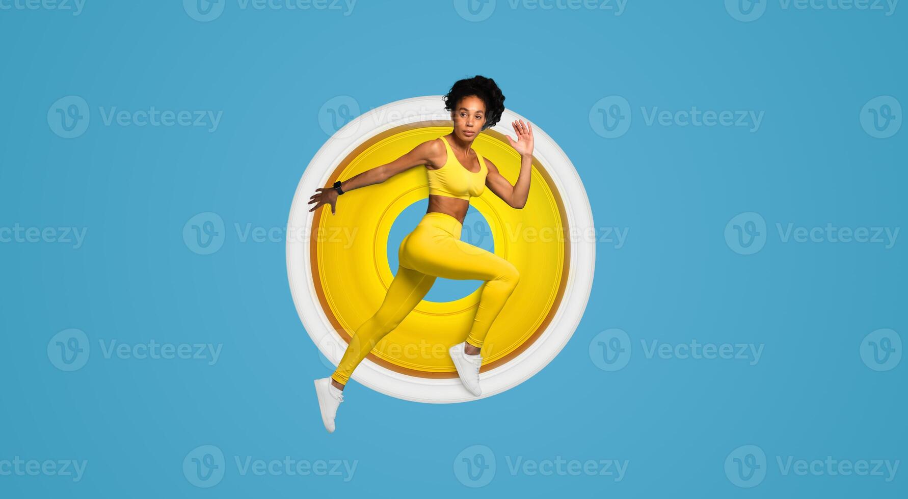 African American woman in action wearing vibrant yellow sports attire performing a jumping pose on a blue background photo