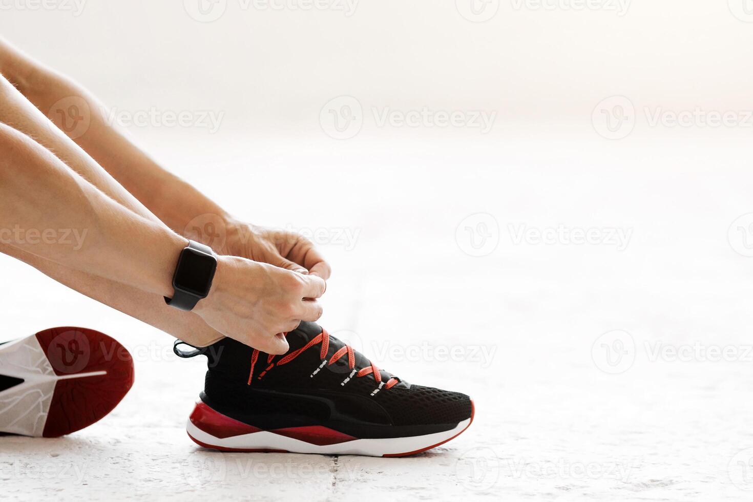 Healthy life, keep fit concept. Woman with fitness tracker tying shoelaces on fashion sneakers, sitting on floor in gym or living room, cropped, copy space photo