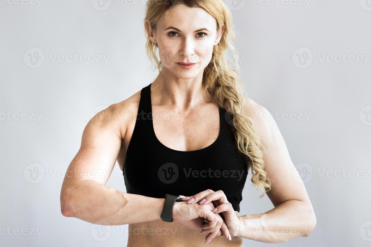 Keep fit during covid-19 lockdown and modern workout in middle age at home loft. Serious slim muscular adult lady in sportswear checking pulse on fitness tracker and look at camera, free space photo