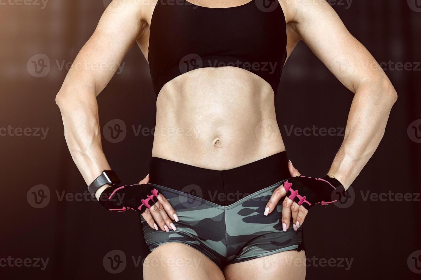 Fit female model with perfect torso in studio. Middle age woman in sportswear, with smart watch and gloves on black background, copy space photo