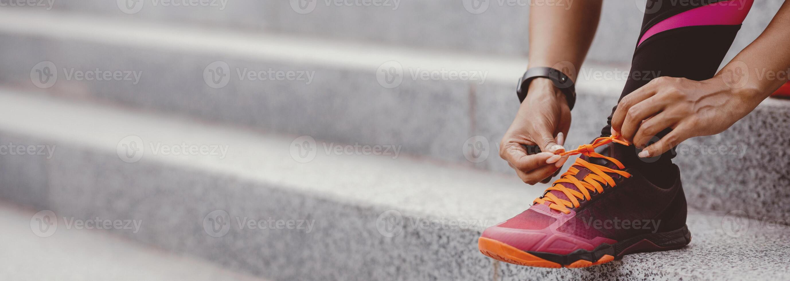 Morning run in city. African american girl with fitness tracker ties shoelaces on fashionable sneakers, close up, panorama, free space photo
