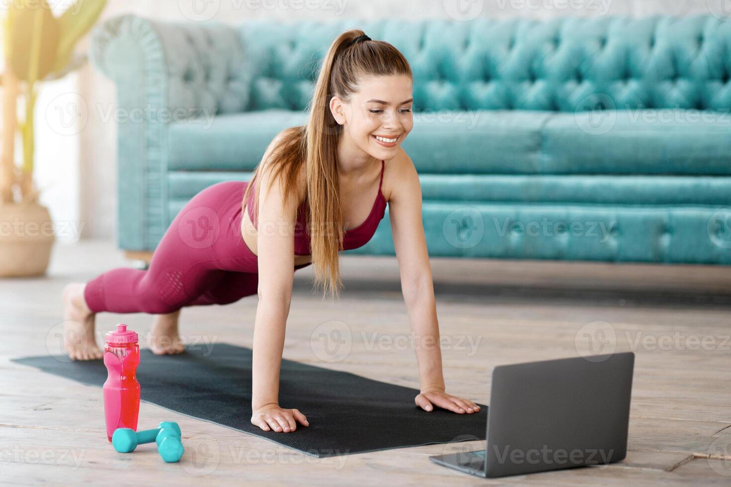 Happy millennial girl doing plank exercise to online class on laptop computer at home photo