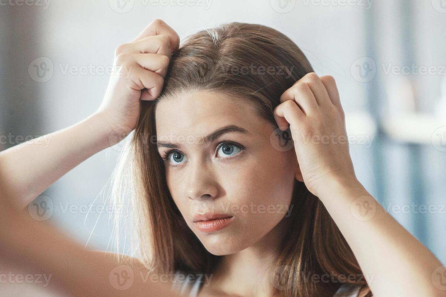 Millennial woman with problematic hair looking in mirror at bathroom, copy space photo