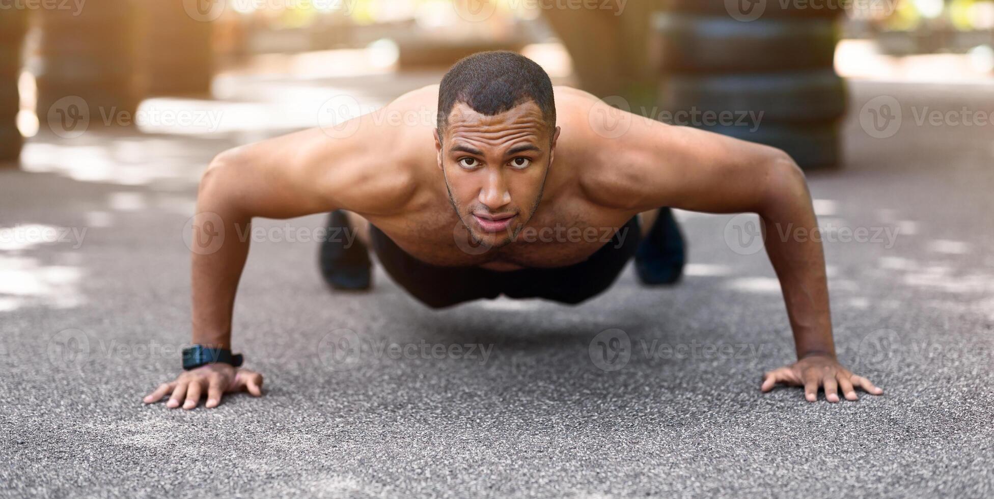 Strong black guy doing push ups or plank exercise after running at park in morning, panorama photo
